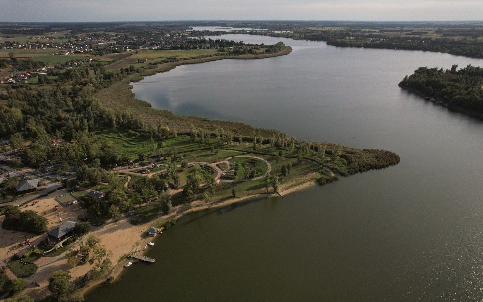 Aerial view of a wooded lakeside park on a peninsula with a sandy beach and pathways