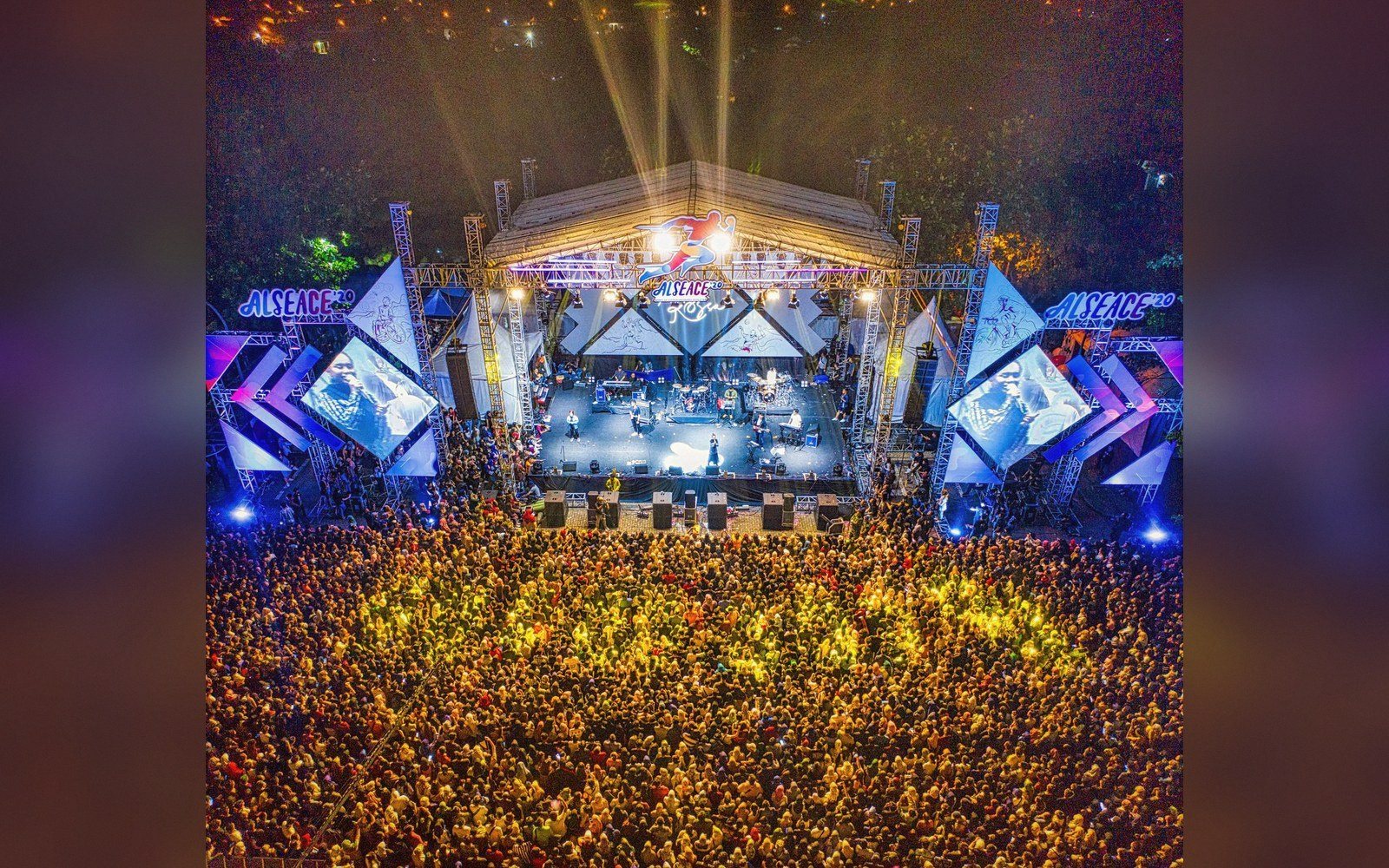 Aerial view of a packed crowd facing an illuminated concert stage at night